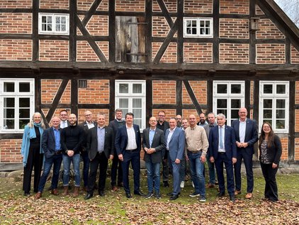 Jahreskonferenz der Hochwasserpartnerschaft Aller Gruppe von etwa 18 Personen vor einem Fachwerkhaus, stehend auf herbstlichem Laub.