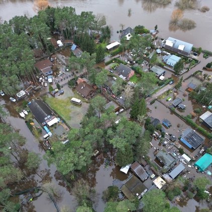 Luftaufnahme von überfluteten Häusern und Bäumen nahe eines Flusses.