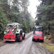 Zwei Traktoren auf einem Waldweg, umgeben von dichtem Wald.