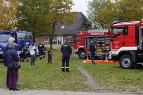 Hochwasseraktionstag Feuerwehrleute stehen vor roten und blauen Einsatzfahrzeugen auf einer Wiese.
