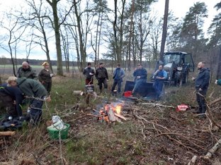Wege freischneiden in Wolthausen und Wittbeck 2025 Gruppe von Menschen um ein Lagerfeuer im Wald, mit Ästen und einem Traktor im Hintergrund.