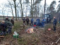 Wege freischneiden in Wolthausen und Wittbeck 2025 Gruppe von Menschen um ein Lagerfeuer im Wald, mit Ästen und einem Traktor im Hintergrund.