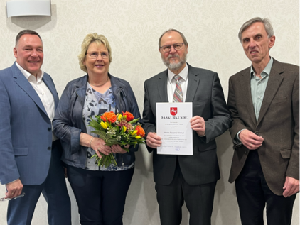 Vier Personen, eine Frau mit Blumenstrauß, ein Mann mit Urkunde.