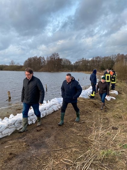 Personen in Gummistiefeln laufen an einem Sandsack-Damm entlang eines Flusses.