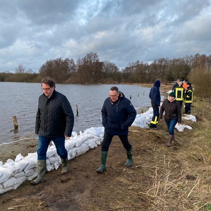 Personen in Gummistiefeln laufen an einem Sandsack-Damm entlang eines Flusses.