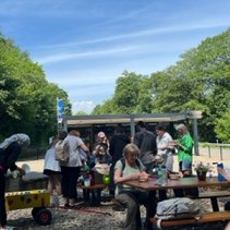 Gruppe von Menschen bei einem Picknick im Freien unter blauem Himmel.