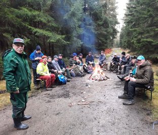Wege freischneiden in Wolthausen und Wittbeck 2025 Gruppe von Menschen sitzt um ein Lagerfeuer im Wald, einige trinken, einer steht lächelnd.