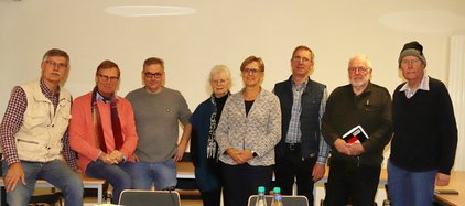 Adventstreffen der Heimatpfleger Eine Gruppe von acht Personen steht lächelnd vor einer weißen Wand.