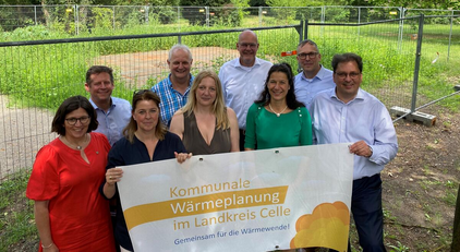 eine Gruppe von Menschen vor einem Bauzaun, die ein Plakat halten