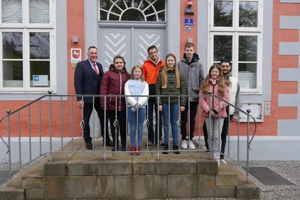 Gruppenfoto von acht Personen unterschiedlichen Alters auf einer Treppe vor einem Gebäude.