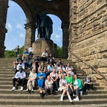 Gruppe von Menschen sitzt auf Treppenstufen vor einer großen Statue.