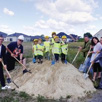 eine Gruppe von Menschen, die um einen Berg von Sand stehen mit Spaten in der Hand