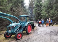 Wege freischneiden in Wolthausen und Wittbeck 2025 Blau-Grüner Traktor mit Anhänger auf Waldweg, dahinter Gruppe von Menschen im Gespräch.