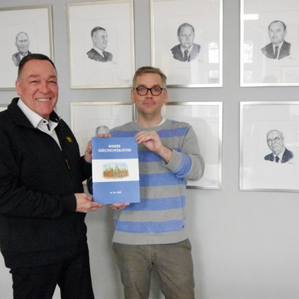 Zwei Männer halten ein Buch mit dem Titel "Winser Geschichtsblätter" vor Porträts.