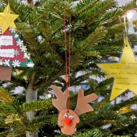 Baumschmuck 2023 Weihnachtsbaum geschmückt mit selbstgebastelten Dekorationen, darunter ein Stern mit der Nachricht "Wir wünschen für die Welt, dass alle Menschen auch mal Schokolade essen können" und ein weiterer Stern mit der Aufschrift "Arabisch" neben einem handgefertigten Rentier.