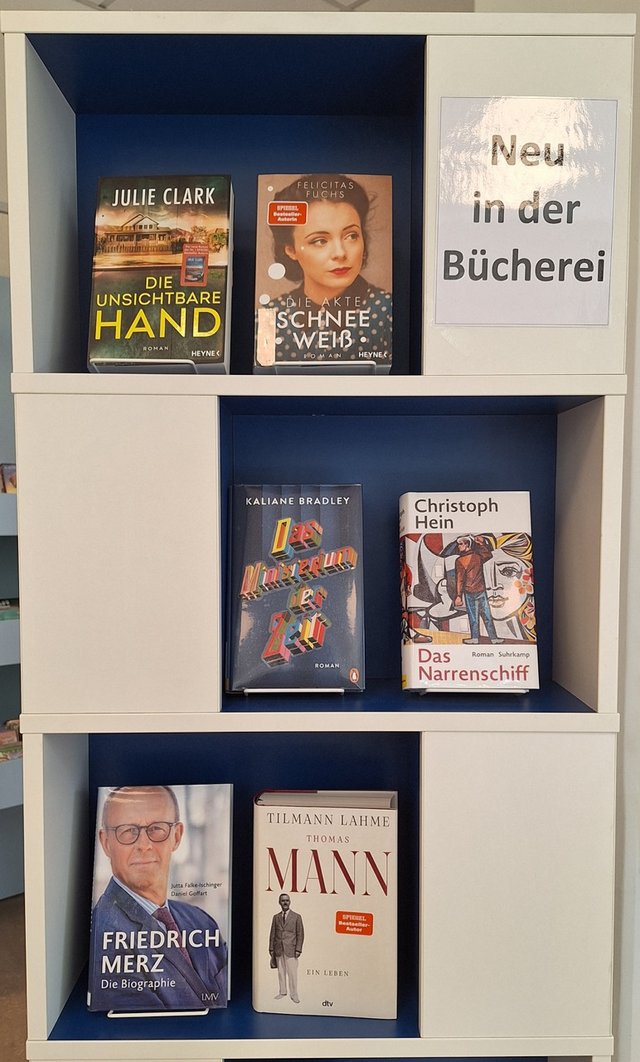 Sechs neue Bücher in einem Regal mit dem Schild „Neu in der Bücherei“, darunter Titel wie „Das Narrenschiff“ und „Thomas Mann“.