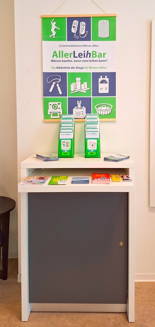 Informationsbereich der AllerLeihBar in Winsen (Aller). Flyer und Broschüren liegen bereit. Im Hintergrund ein Plakat mit dem Logo und dem Slogan 'Warum kaufen,