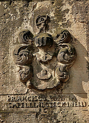 Verwittertes steinernes Wappen mit lateinischer Inschrift darunter, an einer Mauer befestigt.