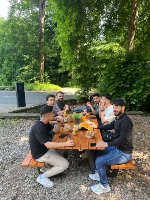 Gruppe von Männern sitzt an einem Picknicktisch im Freien und genießt Getränke.