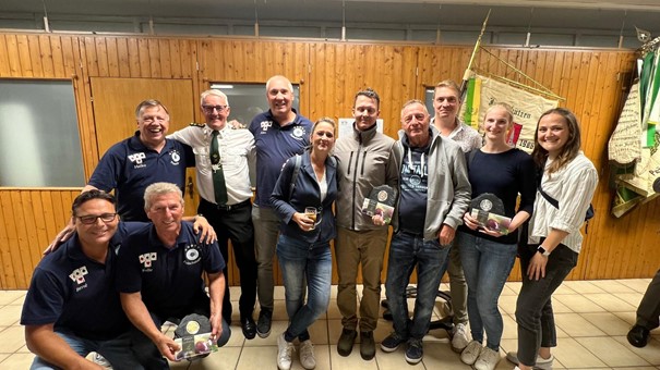 Gruppe lachender Menschen mit Pokalen in einem Raum mit Holzverkleidung.