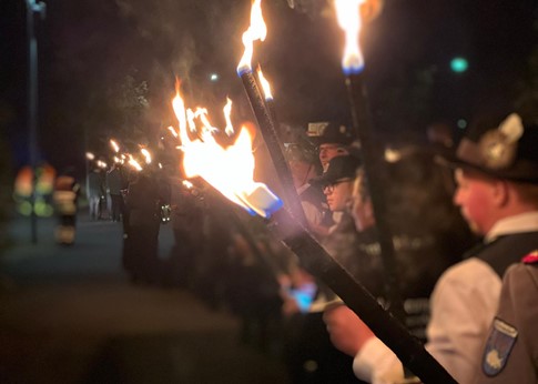 Menschen in Schützenuniformen tragen Fackeln bei einem nächtlichen Umzug.