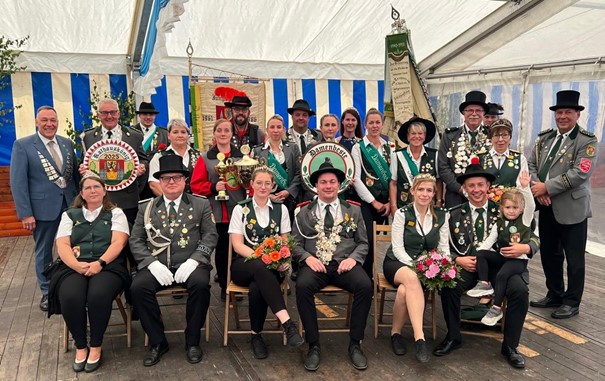 Festlich gekleidete Schützen posieren im Zelt mit Orden, Blumen und Schildern.